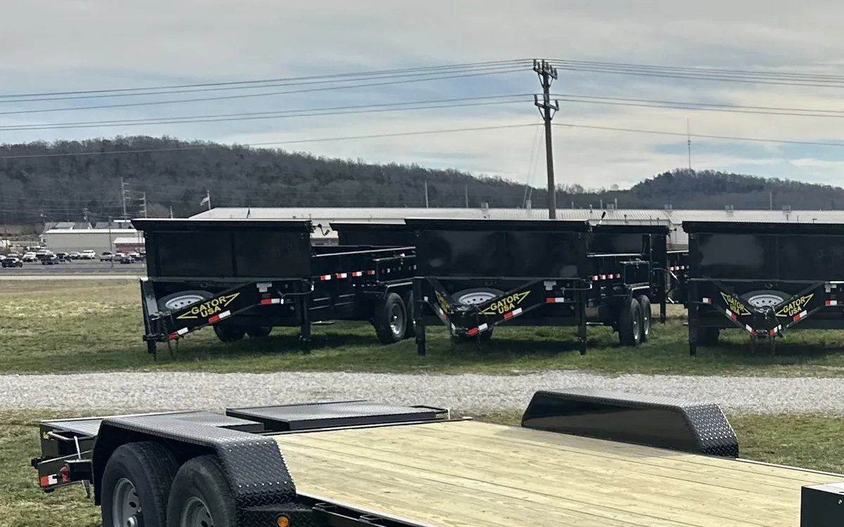 Row of Gatormade dump trailers lined up at the factory yard behind a gooseneck equipment trailer