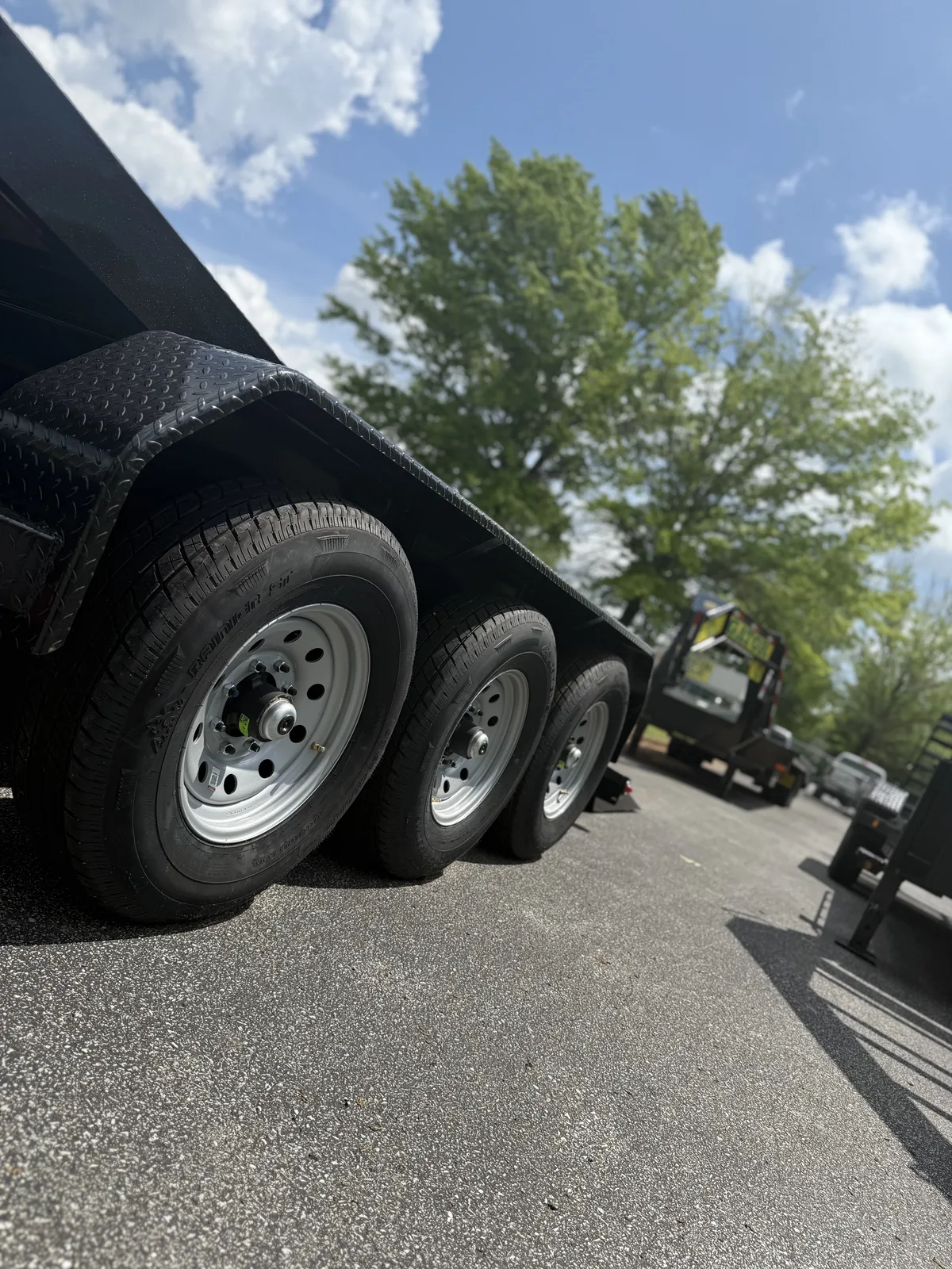 Low-angle view of a triple-axle Gatormade dump trailer with all wheels and brake hubs visible